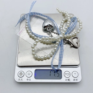 Detail showing pearl keychain with heart pendant and ribbon on a digital scale