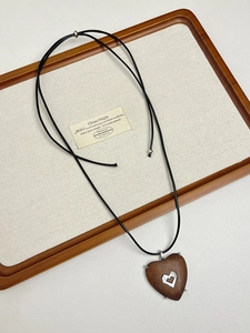 Macro detail of dark wood heart pendant with metallic hollow center on a minimalist necklace