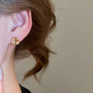 Close-up of a woman wearing gold twisted knot earrings with polished metallic finish