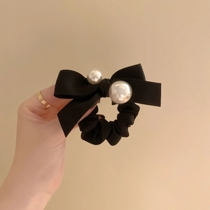 Elegant black silk velvet bow scrunchie with white pearls hair accessory held in hand