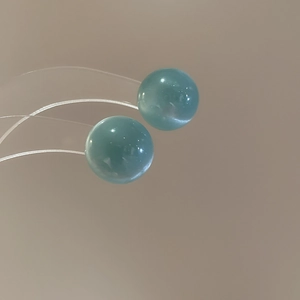 Close-up of cyan blue bead stud earrings with smooth finish and minimalist floral design