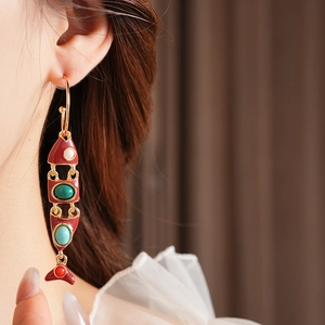 Gros plan d'une boucle d'oreille poisson vintage en or avec émail rouge et gemmes vertes