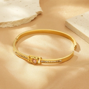 Macro detail of golden heart bangle featuring a pink gemstone and crystal inlay