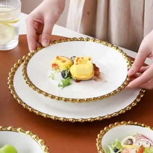 White ceramic plate with gold beaded edge being held, featuring luxury dining style
