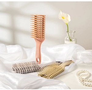 Three vented hair brushes in pink, grey, and beige resting on elegant white silk fabric