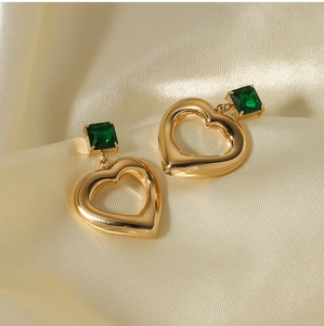 Detailed shot of golden heart earrings with green zircon on soft beige satin fabric