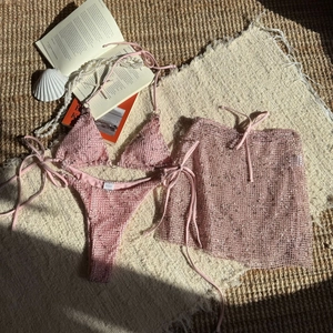 Detailed flat lay of pink glitter mesh three-piece bikini set with wrap skirt and props