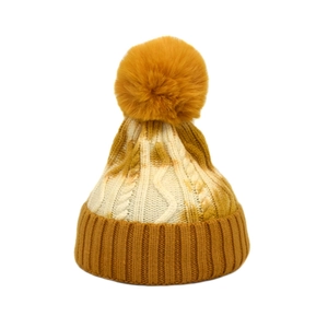Detail of cable knit pattern and large faux fur pompom on tie-dye winter beanie