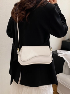 Elegant white leather crossbody bag with wave flap, worn with black blazer and white skirt