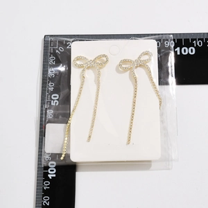 Detail view of gold bow earrings with white rhinestones and length measurement of 65mm