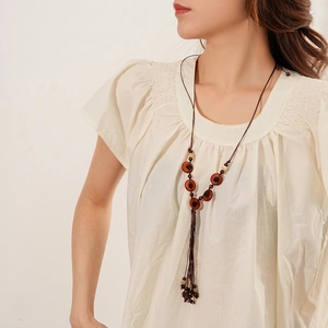 Bohemian woven wood bead long necklace with vintage tassel pendant on white shirt