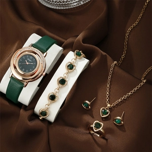 Elegant gold watch and green heart jewelry set displayed on brown silk fabric