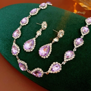Detail of luxury jewelry set with purple waterdrop gems and diamonds on green velvet