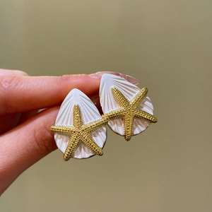 Detailansicht eleganter goldener Seestern und weißer Muschel Tropfenohrringe in der Hand