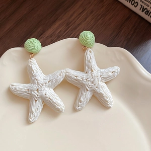 Detail of woven white starfish earrings with green circular accents on ceramic plate