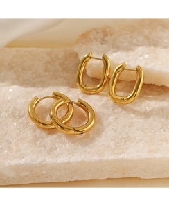 Close-up of polished gold circular and oval geometric earrings on stone surface