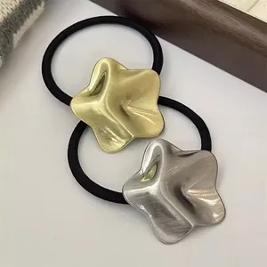 Detailed view of two minimalist star metal pendants on black elastic hair ties in gold and silver