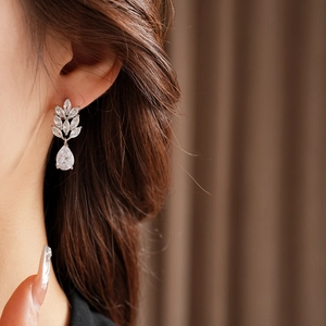 Macro side view of silver teardrop earrings with white zircon on a model's ear