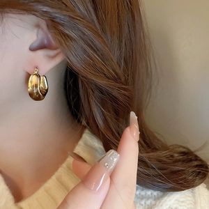 Close-up of elegant gold U-shaped resin amber earrings on a model wearing white knitwear