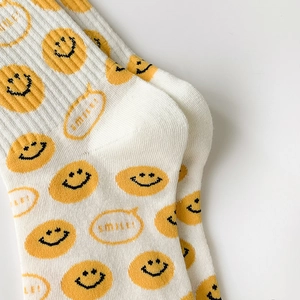 Detailed macro view of white cotton mid-calf socks with yellow smile face and knit texture