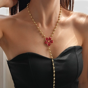 Detail of a gold beaded Y-shaped necklace with a red floral pendant on a fashion model