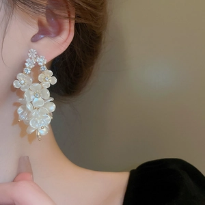 Close-up of white acrylic flower drop earrings with rhinestones worn by a model