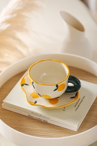 Macro shot of cream ceramic tea cup and saucer with creative hand-painted lemon pattern