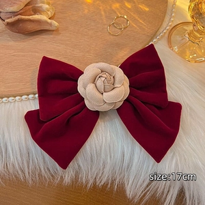 Detail of a large red velvet bow hair clip with a cream rose, measuring 17cm in width