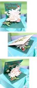 Detailed view of 3D pop-up birthday card featuring white paper flowers and gold foil text