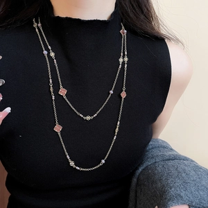 Detail of layered gold necklace with pink flower charms on a black sweater
