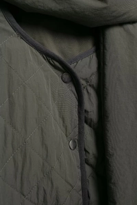 Close-up of diamond-quilted army green jacket featuring snap buttons and black piping edges