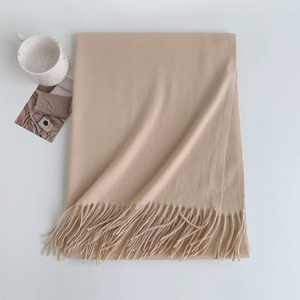 Flat lay of a soft beige fringed scarf with a cozy ceramic mug and decorative card