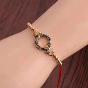 Detailed close-up of a red cord bracelet with gold ring and blue zircon inlays