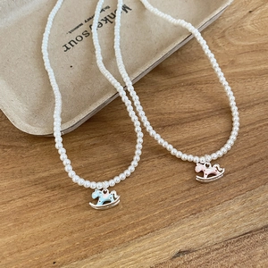 Detail view of pearl necklaces with colorful rocking horse pendants on a minimalist tray