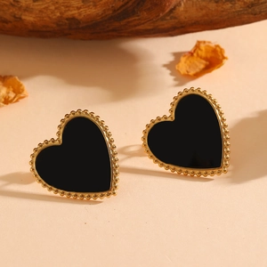 Detail of heart-shaped black shell earrings with gold beaded edges on a natural background
