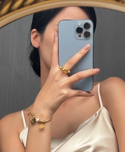 Detail of beaded gold ring and heart charm bracelet set worn by a model in mirror view