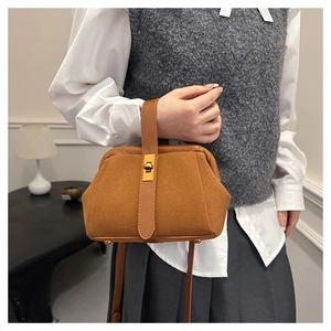 Detailed shot of brown frosted shell handbag with metal clasp held by model