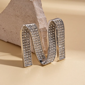 Silver-tone letter M brooch with sparkling rhinestones on a natural stone background