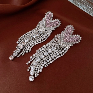 Close-up of heart-shaped silver earrings with pink zircon and sparkling tassel detail