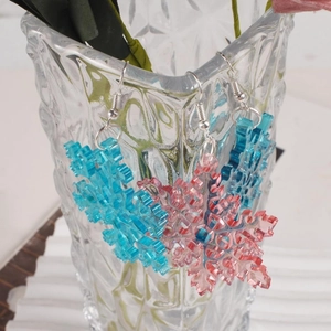 Detail of blue and pink snowflake resin earrings hanging on a glass vase edge