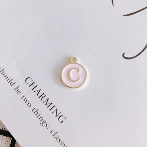 Macro detail of round pink enamel pendant with golden letter C and hanging loop