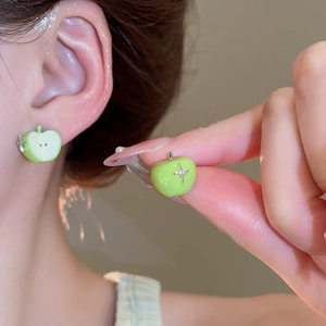 Close-up of green apple stud earrings with star detail worn on the earlobe