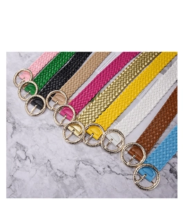 Flat lay of woven belts in multiple colors with gold round metal buckles on marble