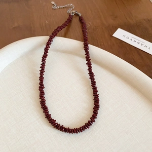 Detail of dark red beaded necklace on cream ceramic tray with a wooden tabletop background