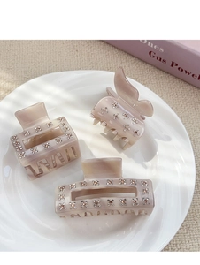 Detailed view of beige acetate hair claws with rhinestones on a ceramic display