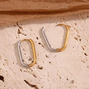 Detail of minimalist two-tone oval hoop earrings on a natural stone aesthetic background