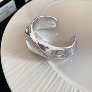 Macro shot of silver liquid metallic open bangle on textured ceramic plate detail