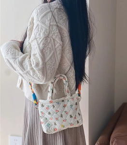 Close-up of quilted floral crossbody bag with colorful woven strap on person