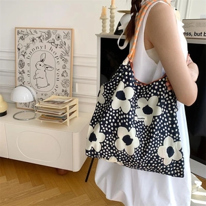 Floral canvas tote bag in navy blue shown on shoulder in a warm studio setting