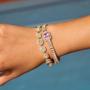 Détail de bracelets dorés empilés avec zircons en cœur et pierre rose rectangulaire